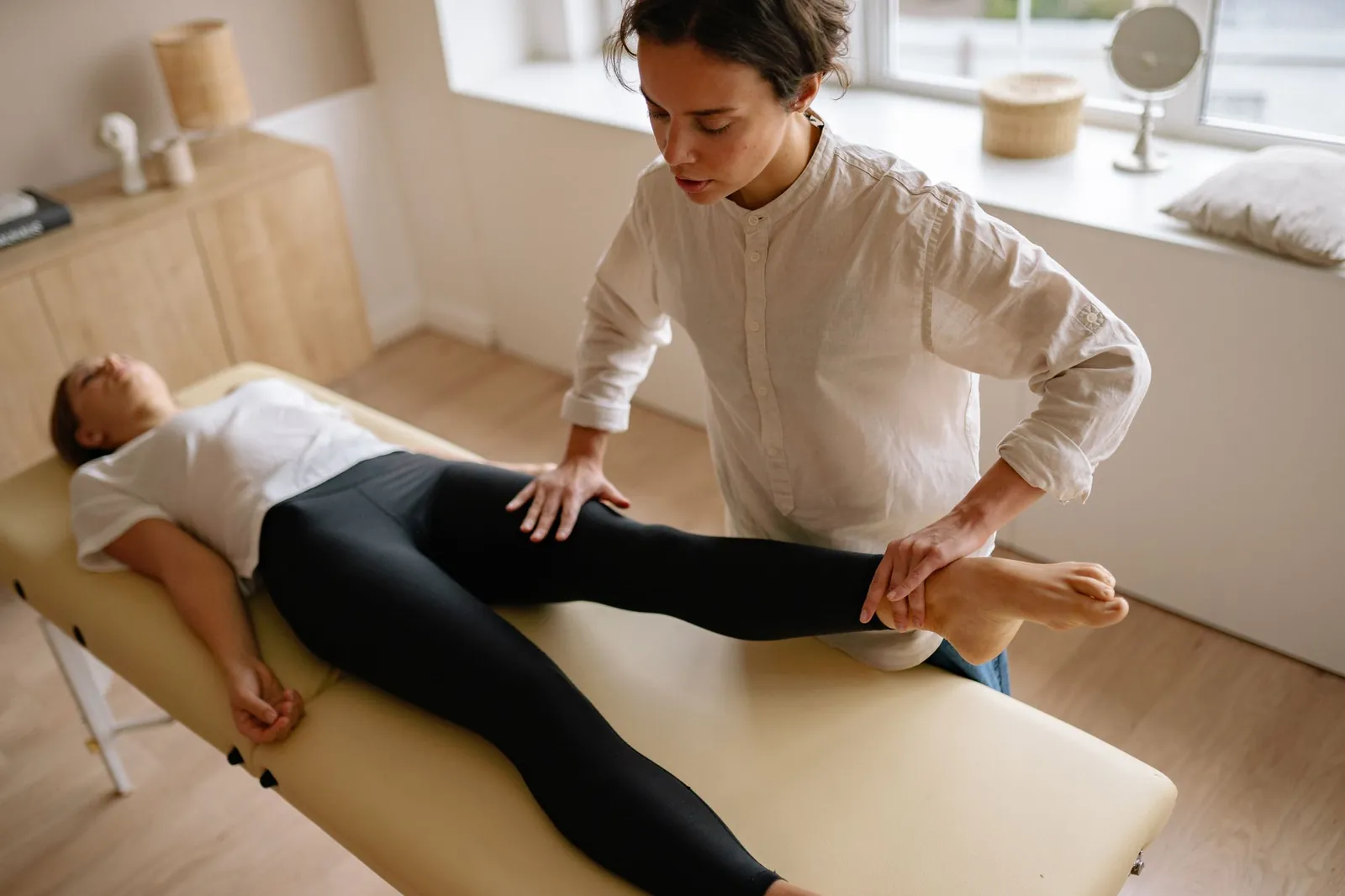Therapeutin mobilisiert das Bein einer liegenden Patientin